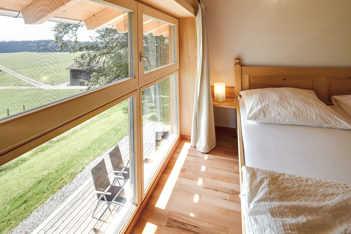 /files/dateien/H%C3%A4user/Kundenh%C3%A4user/Schiefer/doppelhaus-holzhaus-schiefer-wohnraum-holzbalkendecke-holzboden-landhaus-ausblick-schlafzimmer.jpg
