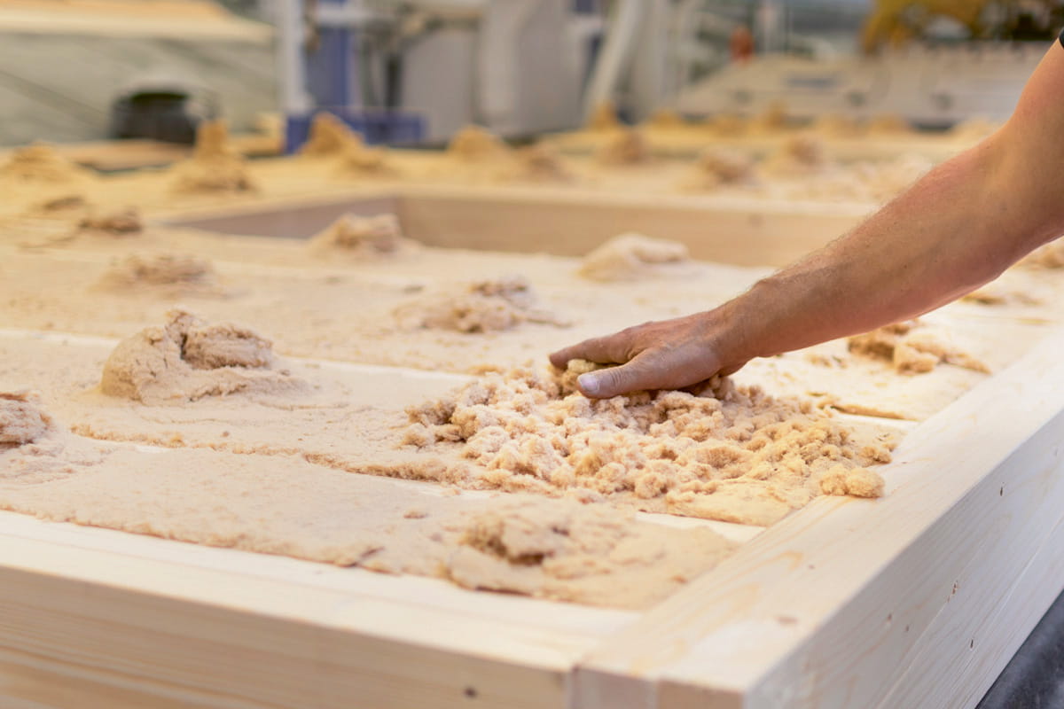 Mann dämmt ein Wand eines Holzständerhauses mit Holzfaserdämmung.